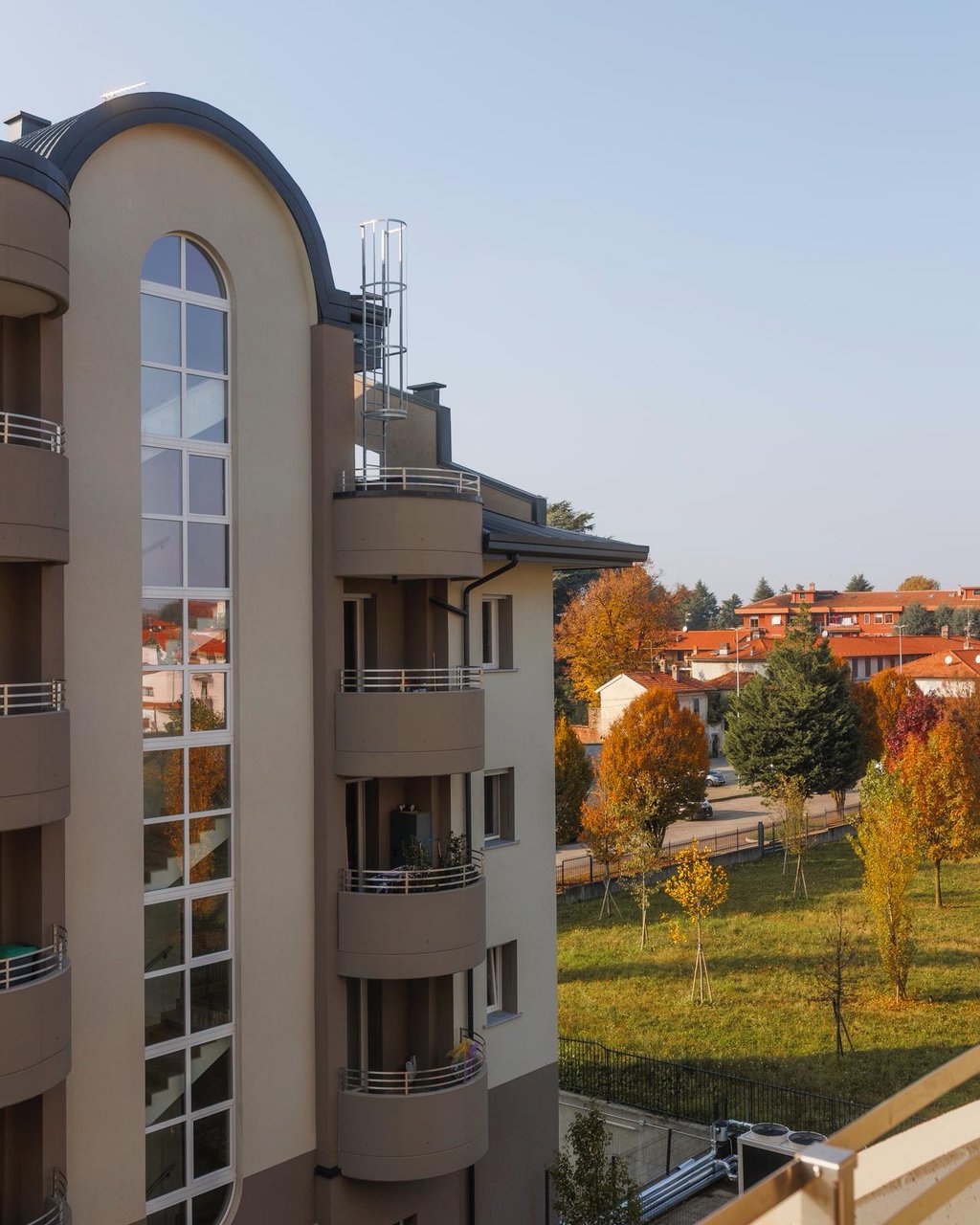 Facciata del Residence La Fenice con la grande vetrata ad arco e i balconi curvi, tra il verde d'autunno di Gorla Minore