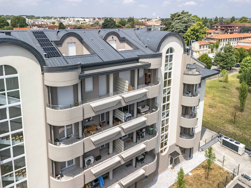 Foto reale dal drone del Residence La Fenice a Gorla Minore: la torre vetrata ad arco, i balconi curvi e il verde attorno